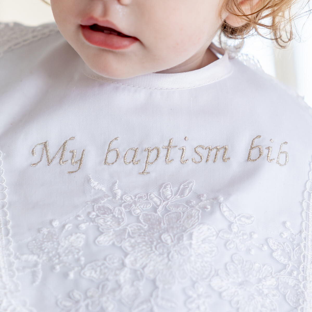 Close-up of a baby's bib with embroidered text and lace details.