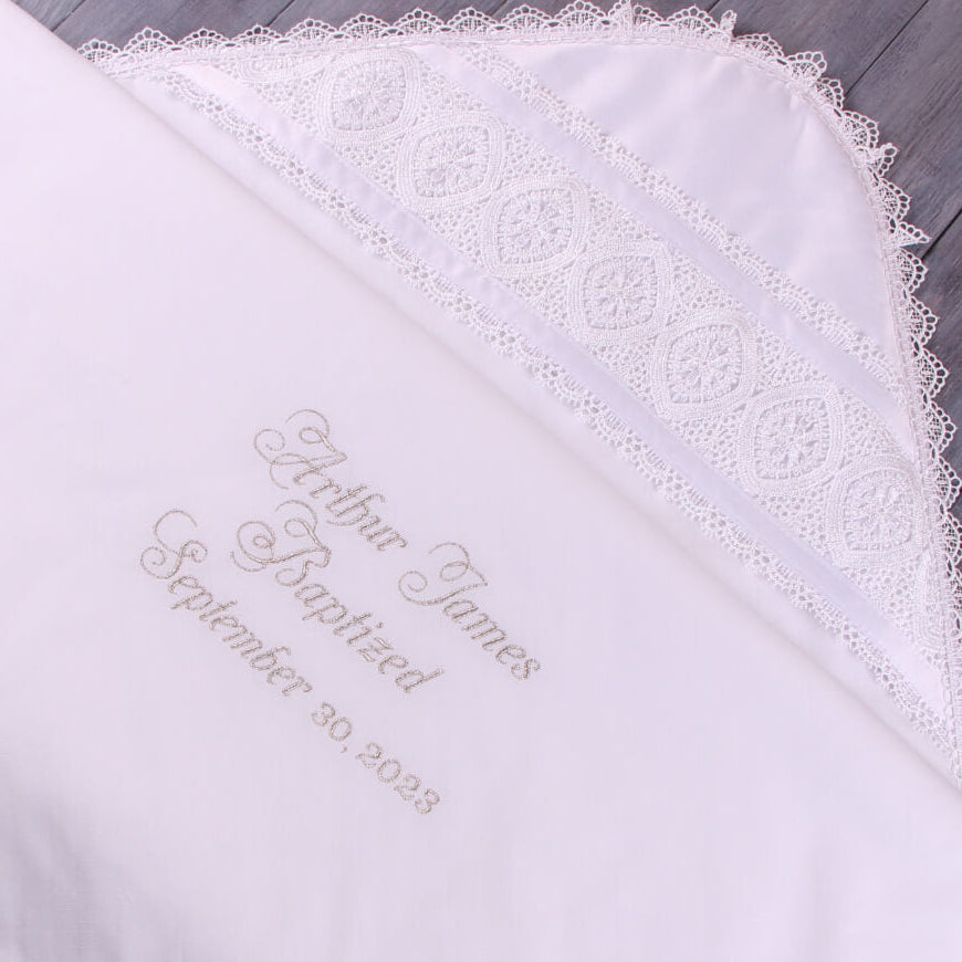 White embroidered blanket with lace trim on a wooden surface