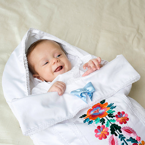 Baby wrapped in Newborn Sleep Sack for Summer with floral embroidery on a light background