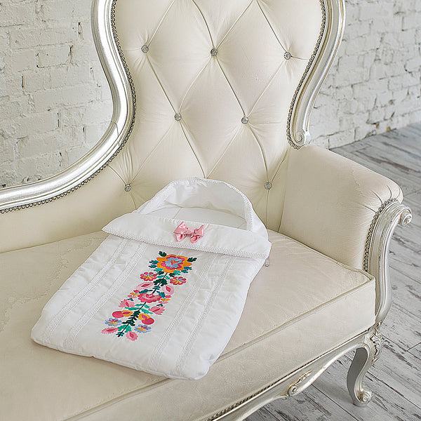 White baby swaddle with floral embroidery on a decorative chair.