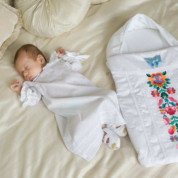 Newborn baby in Newborn Sleep Sack for Summer lying on a beige blanket next to a floral embroidered blanket.