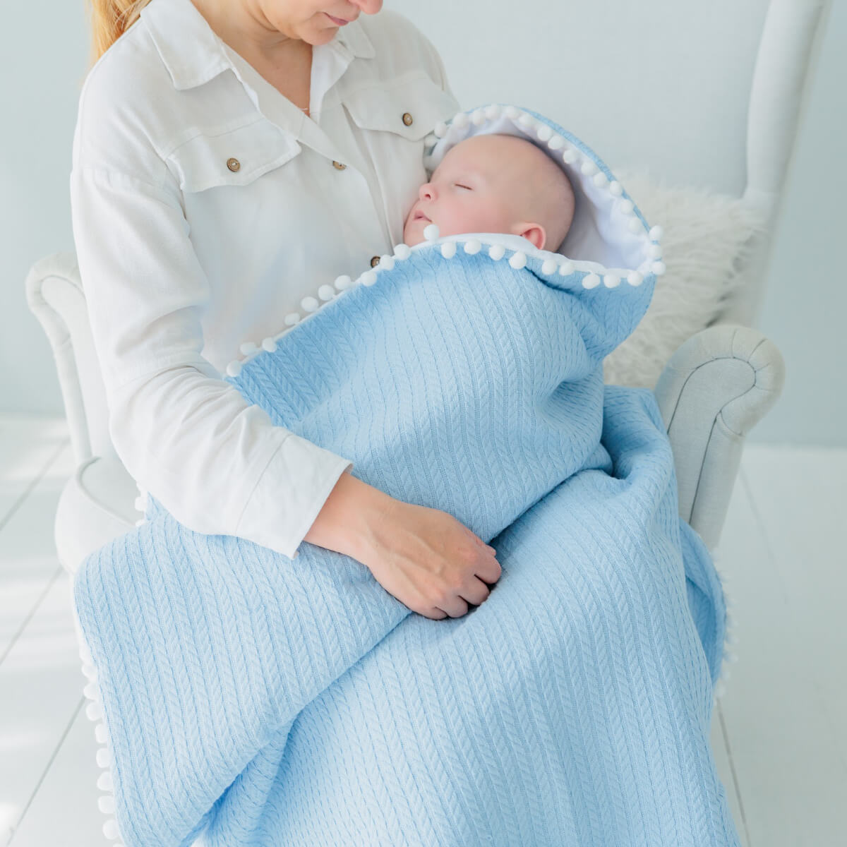Person holding a baby wrapped in a Coming Home Blanket with white trim.