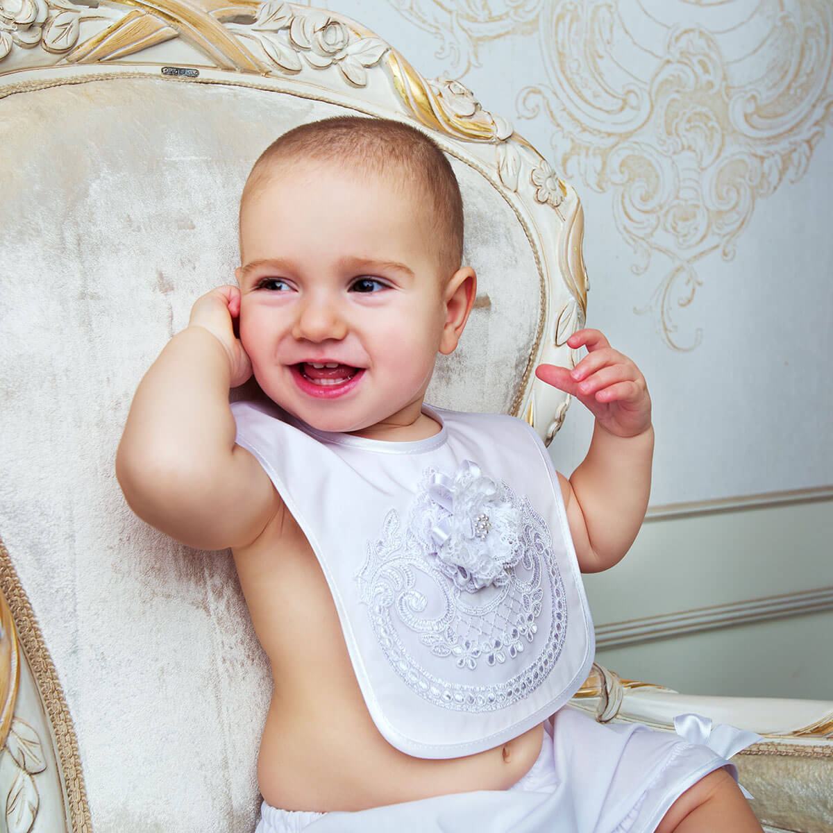 Baptism Bib with Floral Lace with decorative patterns, sitting on an ornate chair.