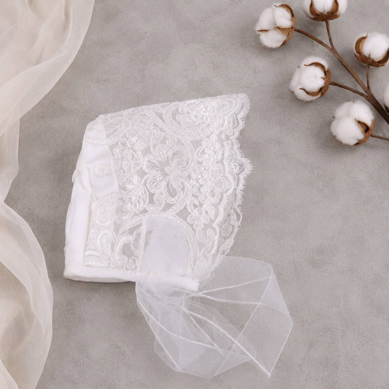 White lace bonnet with a sheer fabric on a gray surface with cotton flowers.