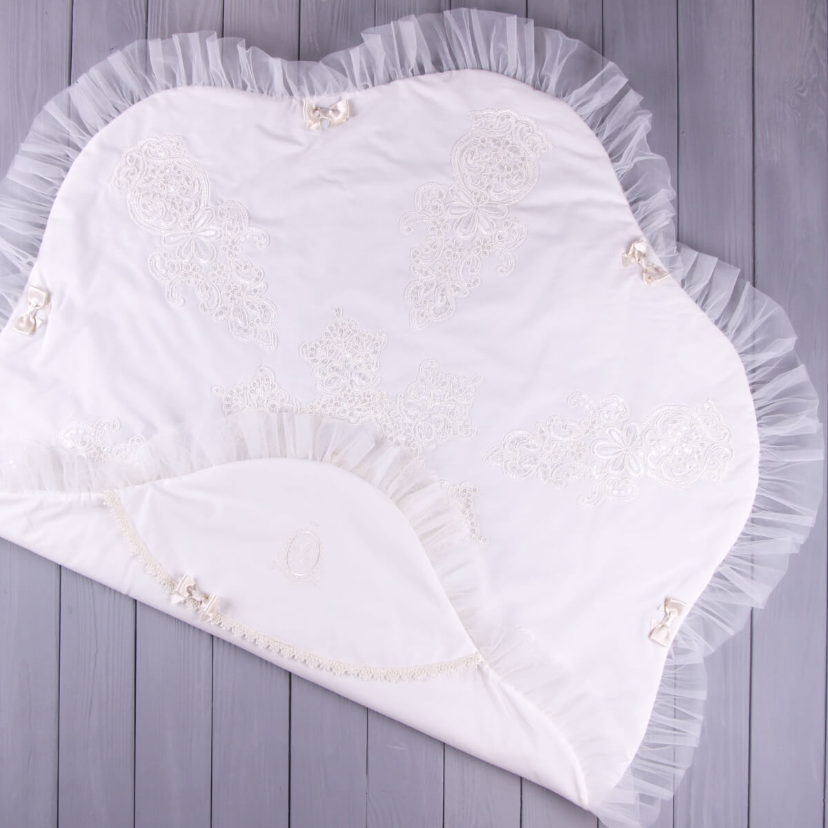 Flower-shaped christening blanket with lace and pearl embellishments on a wooden surface