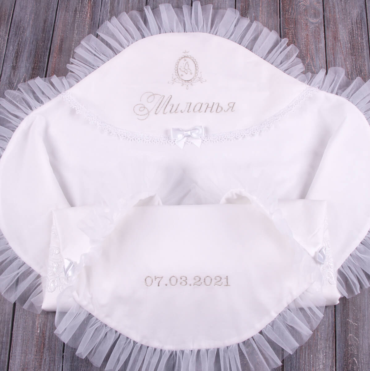 White baby blanket with lace trim and embroidered text on a wooden surface