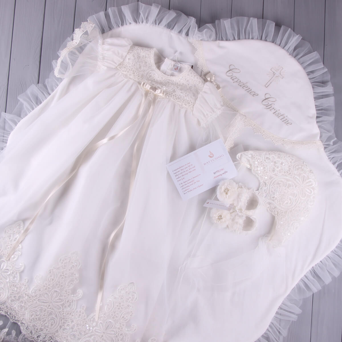 White lace baby gown with matching bonnet on a gray surface