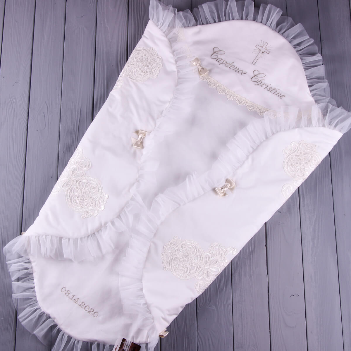 White baby blanket with lace details and embroidery on a wooden surface