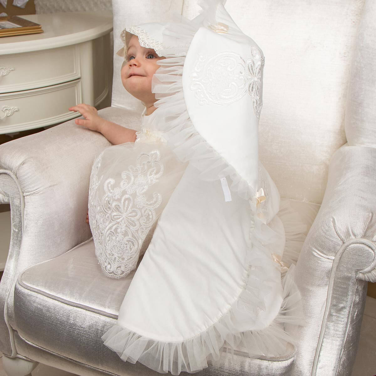 Baby in a Flower-shaped christening blanket sitting on a decorative chair