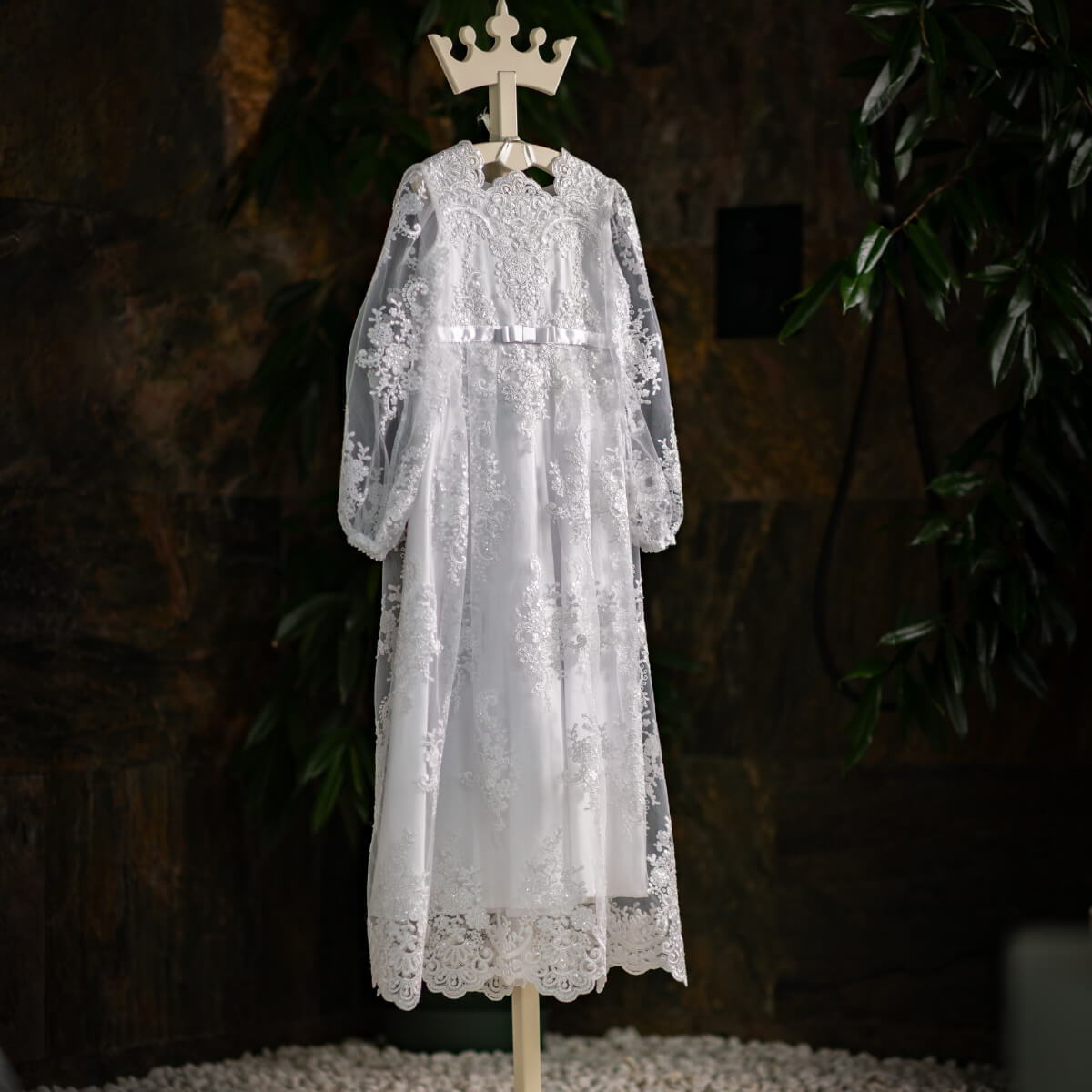 White lace Simple Lace Communion Dress on a mannequin against a dark background with plants.