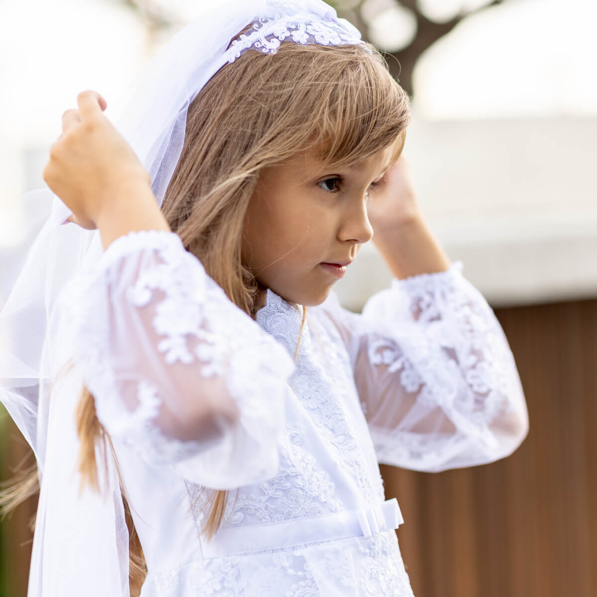 Young girl wearing a white lace dress and headscarf outdoors
