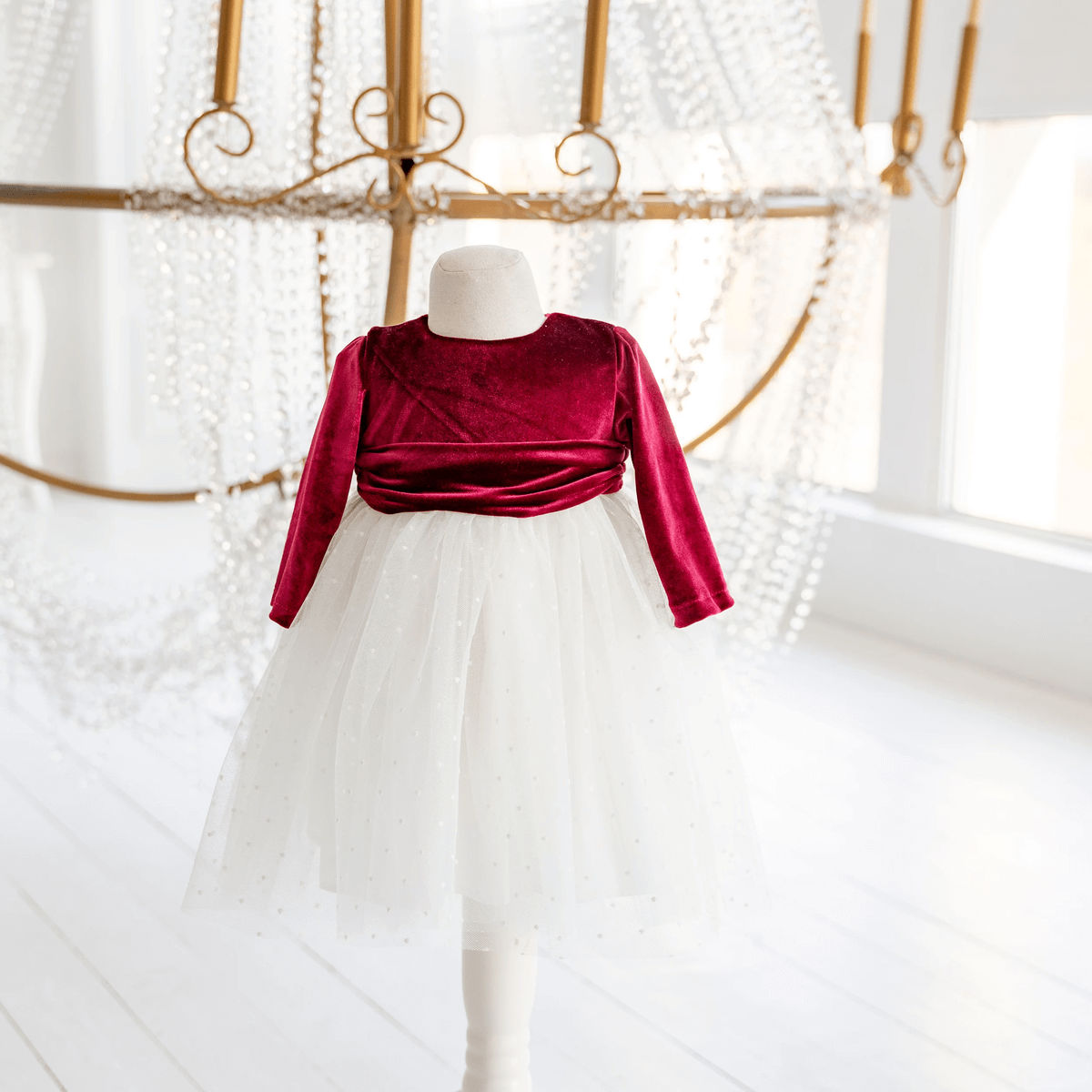 Mannequin wearing a red velvet top and white tulle skirt against a decorative background