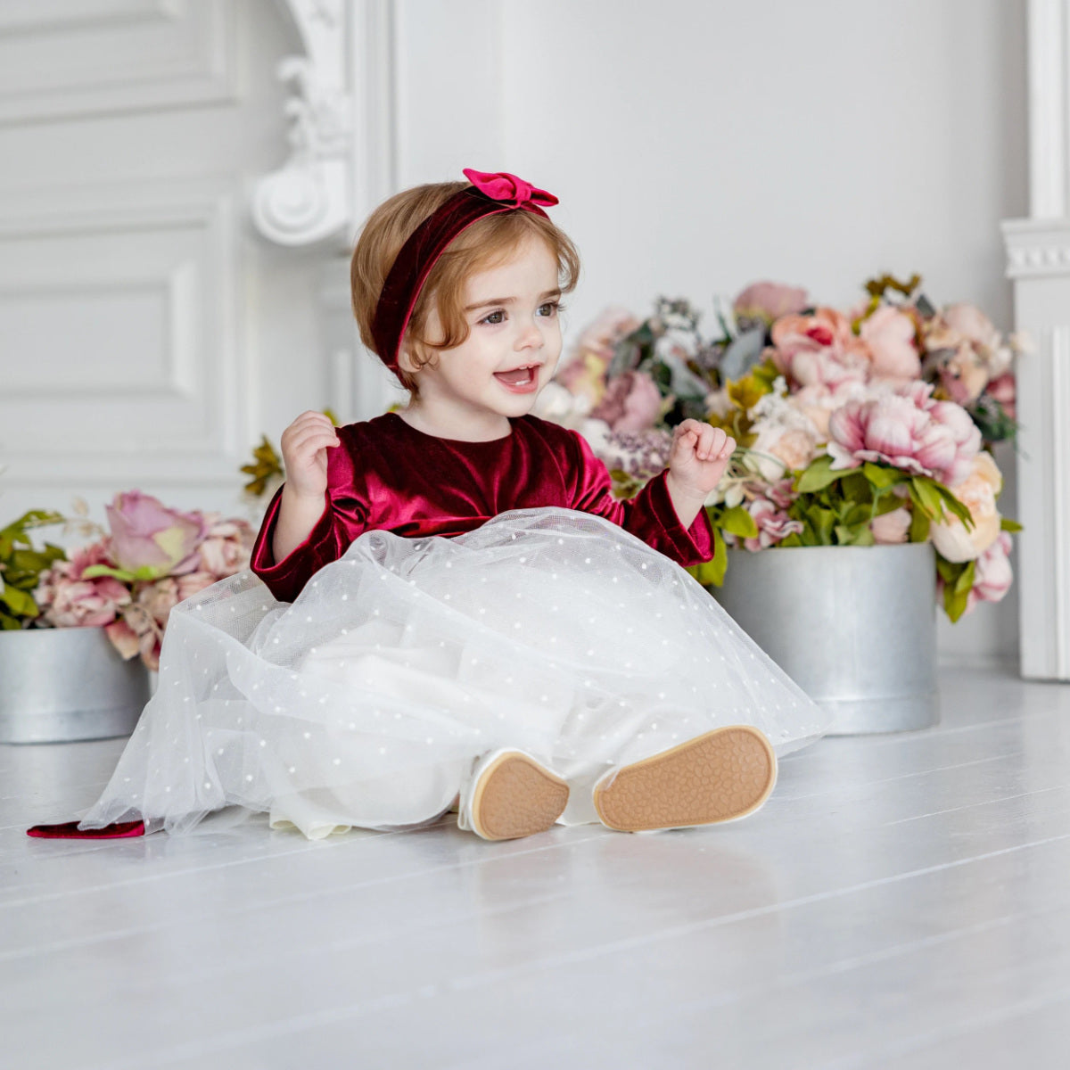 Child in a red and white dress sitting on a white floor with floral decorations.