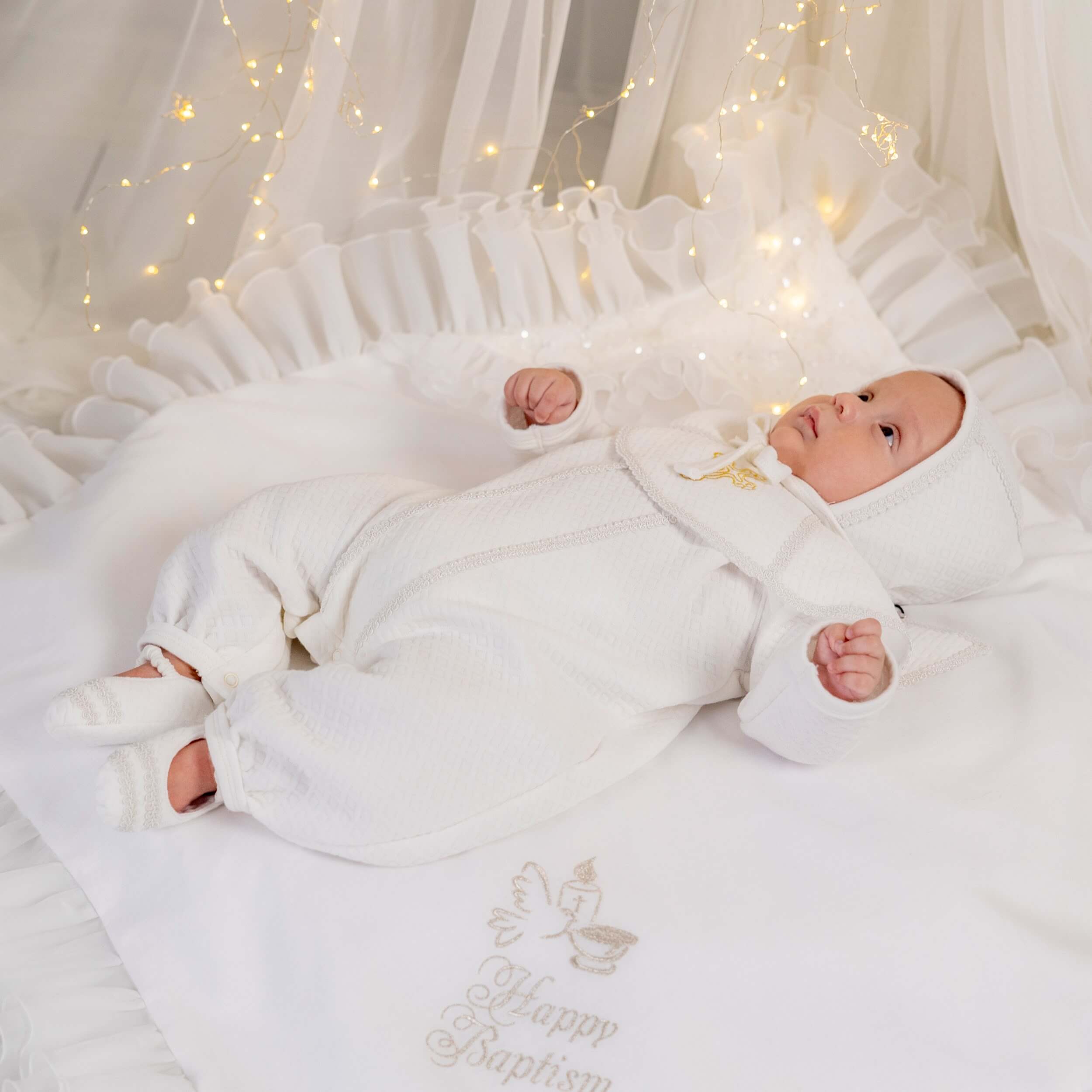  Baptism Outfit for Boys lying on a white blanket with embroidered text, surrounded by fairy lights.