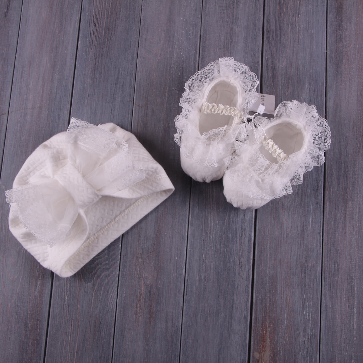 White lace baby shoes and headband  of Baptism Romper Set on a wooden surface