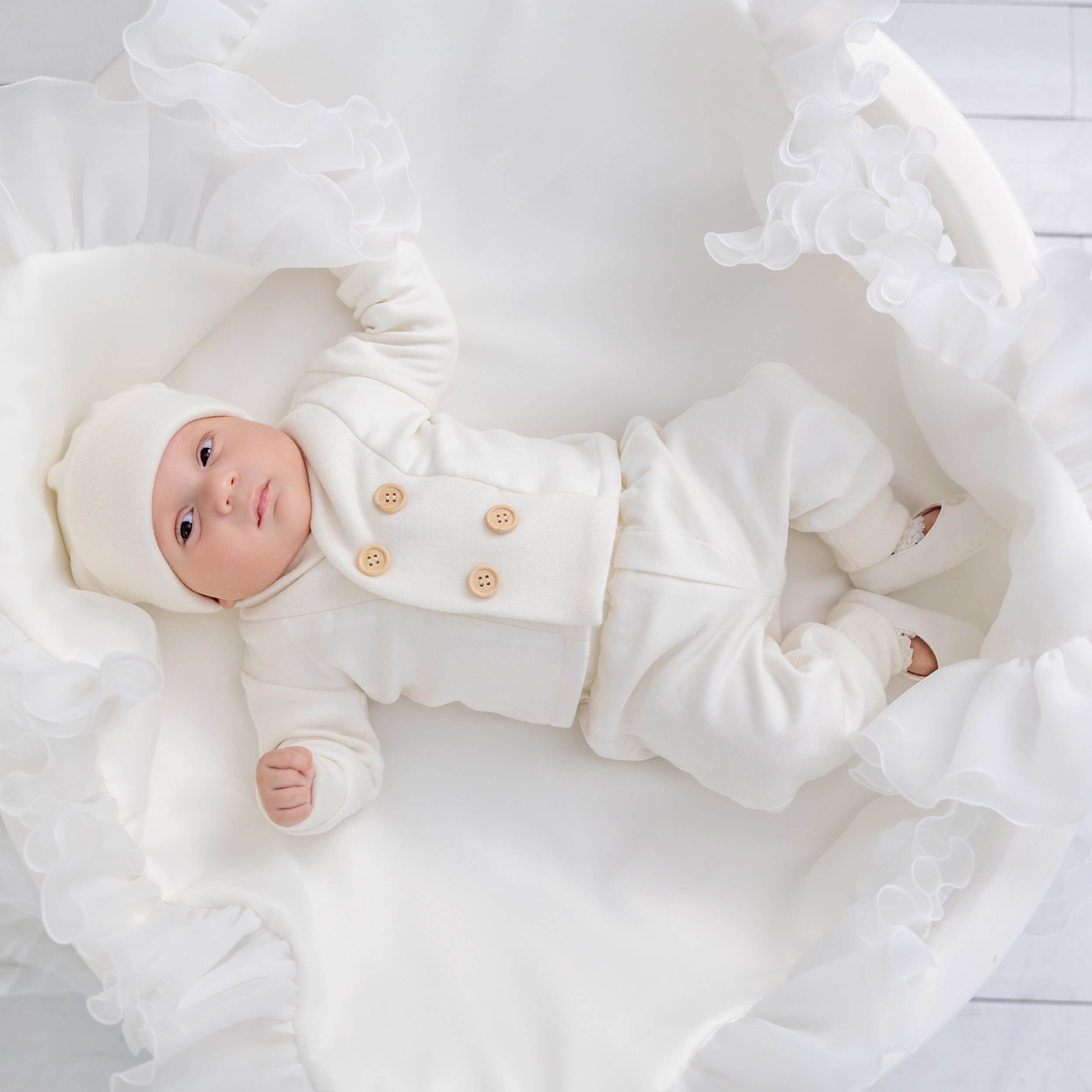 Baptism outfit for boys in a white outfit with buttons, lying on a white blanket.