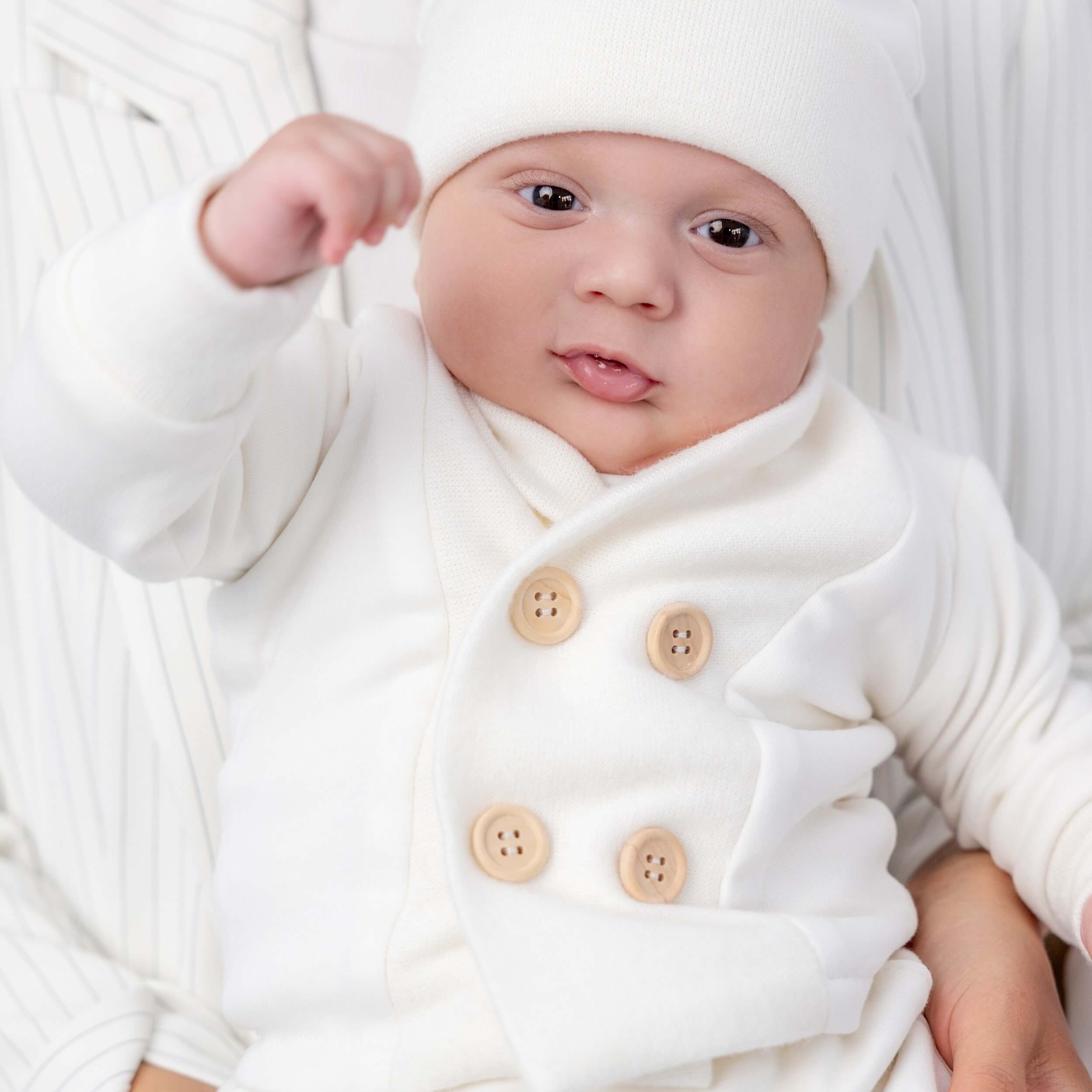 Baby wearing a baptism outfit for boys with brown buttons on a light background