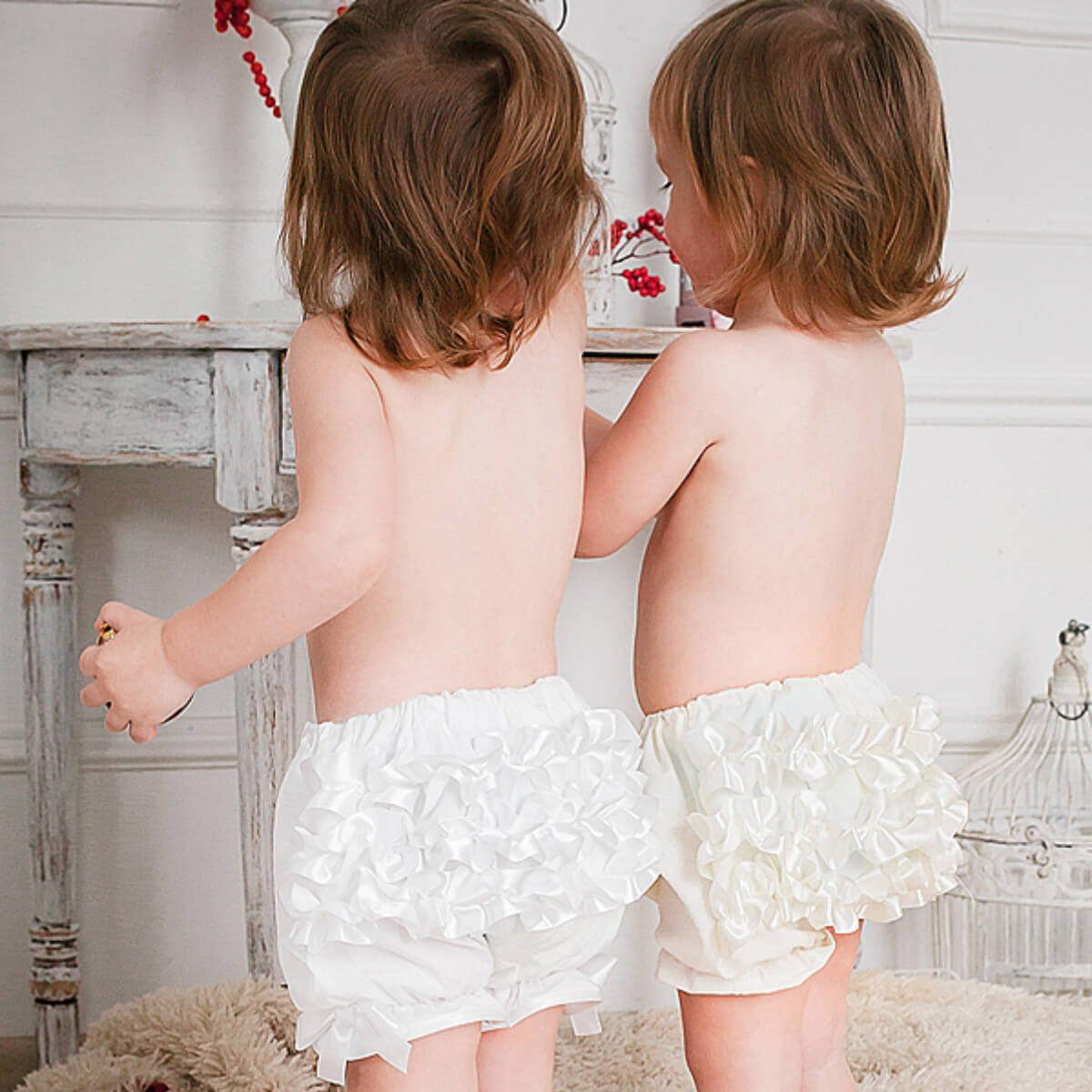 Two children wearing Baby Keepsake Bloomers standing back-to-back in a softly lit room.