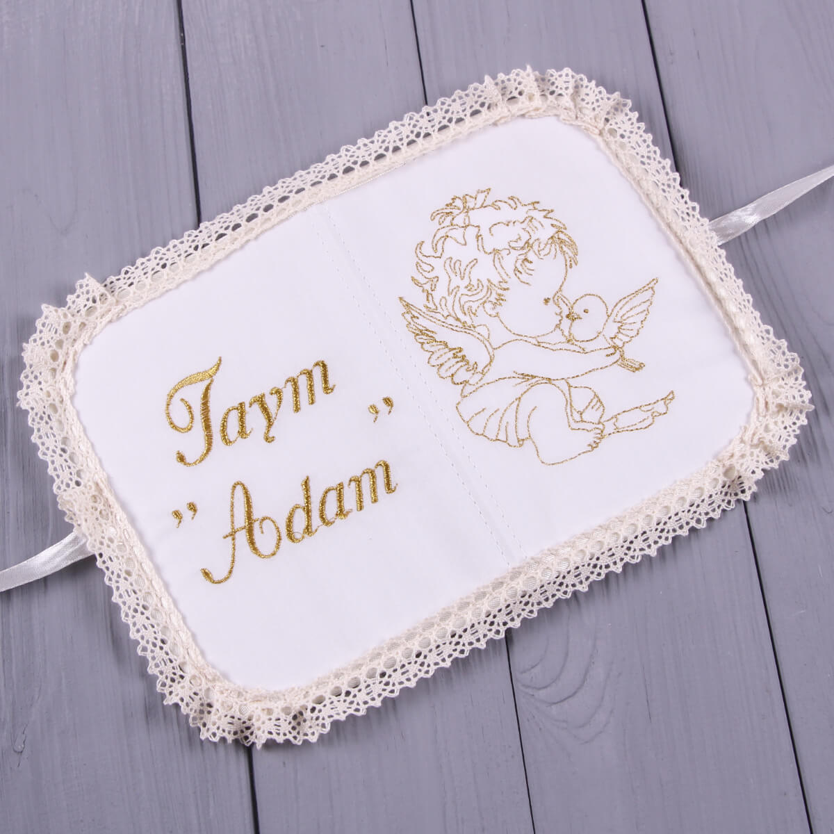 Embroidered angel design on a white fabric with lace trim and embroidered names on a wooden surface.