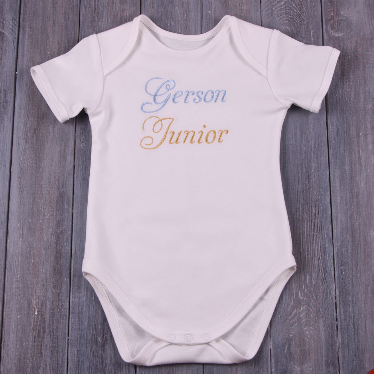 Coming Home Bodysui with 'Gerson Junior' text on a wooden surface