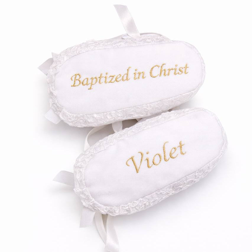 White baby booties with lace details and embroidered text on a white background