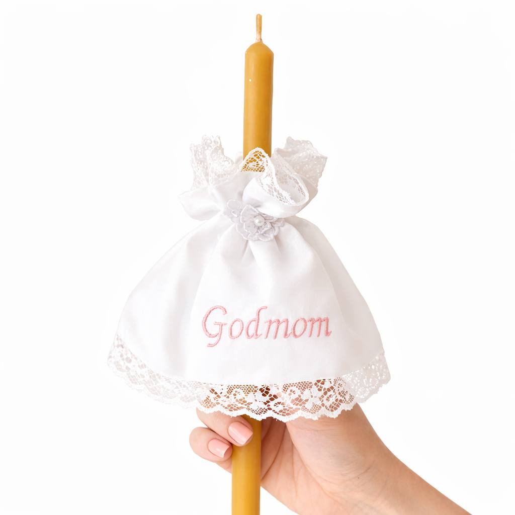 Candle with a lace cover and 'Godmom' embroidery held by a hand on a white background