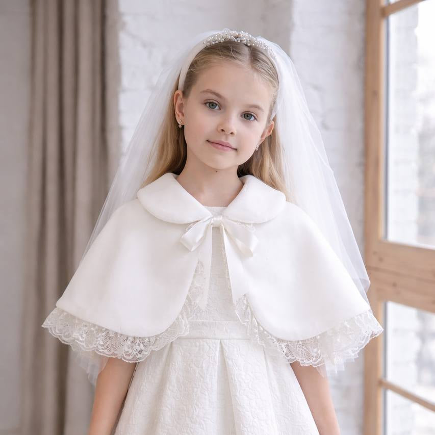 Young girl wearing a white dress with a cape and veil indoors.