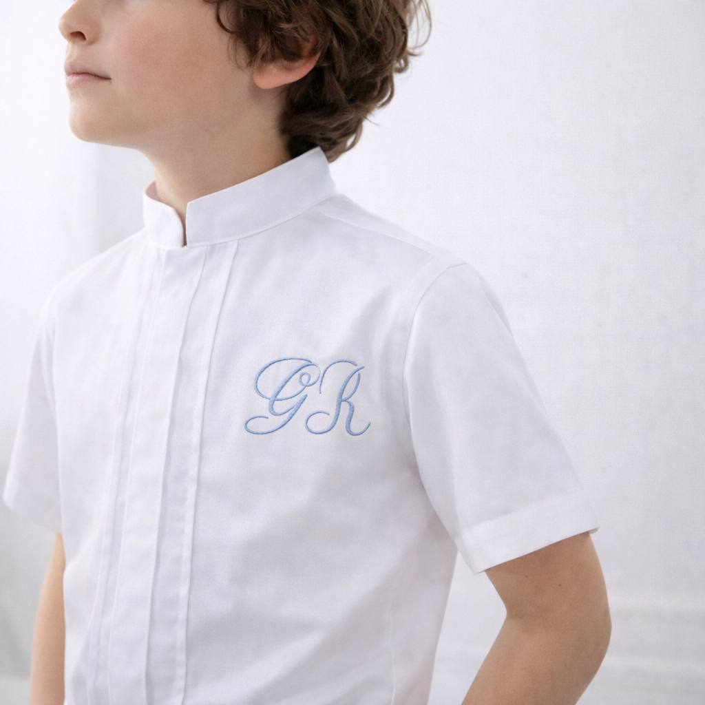Child wearing a white shirt with blue monogram on a plain background