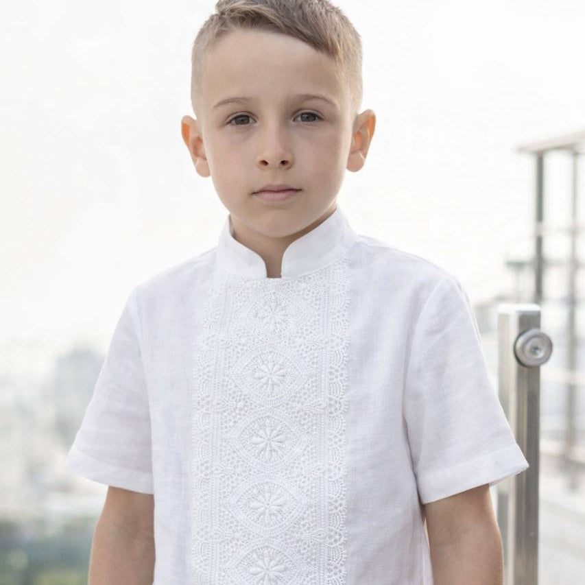 Young boy wearing a white textured shirt with a blurred outdoor background