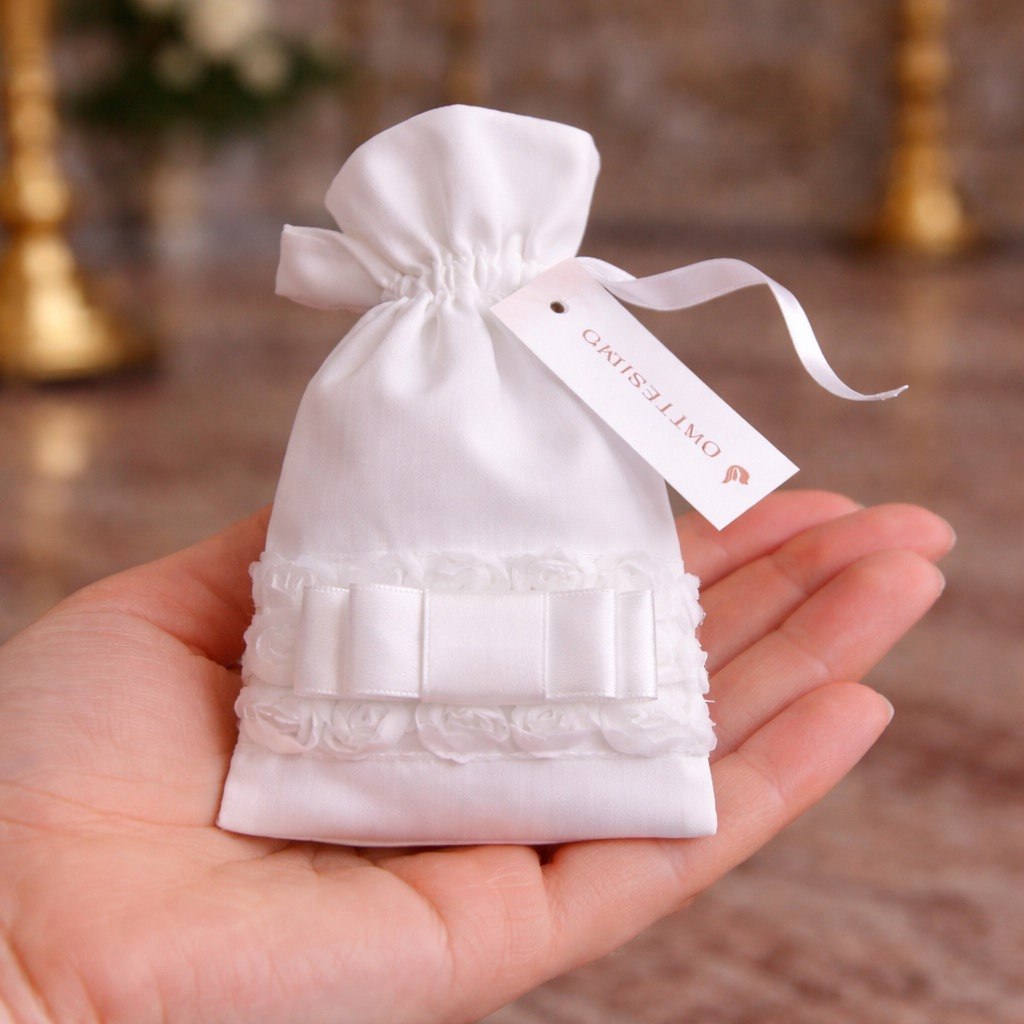 White drawstring bag with lace detail held in a hand, against a blurred background.