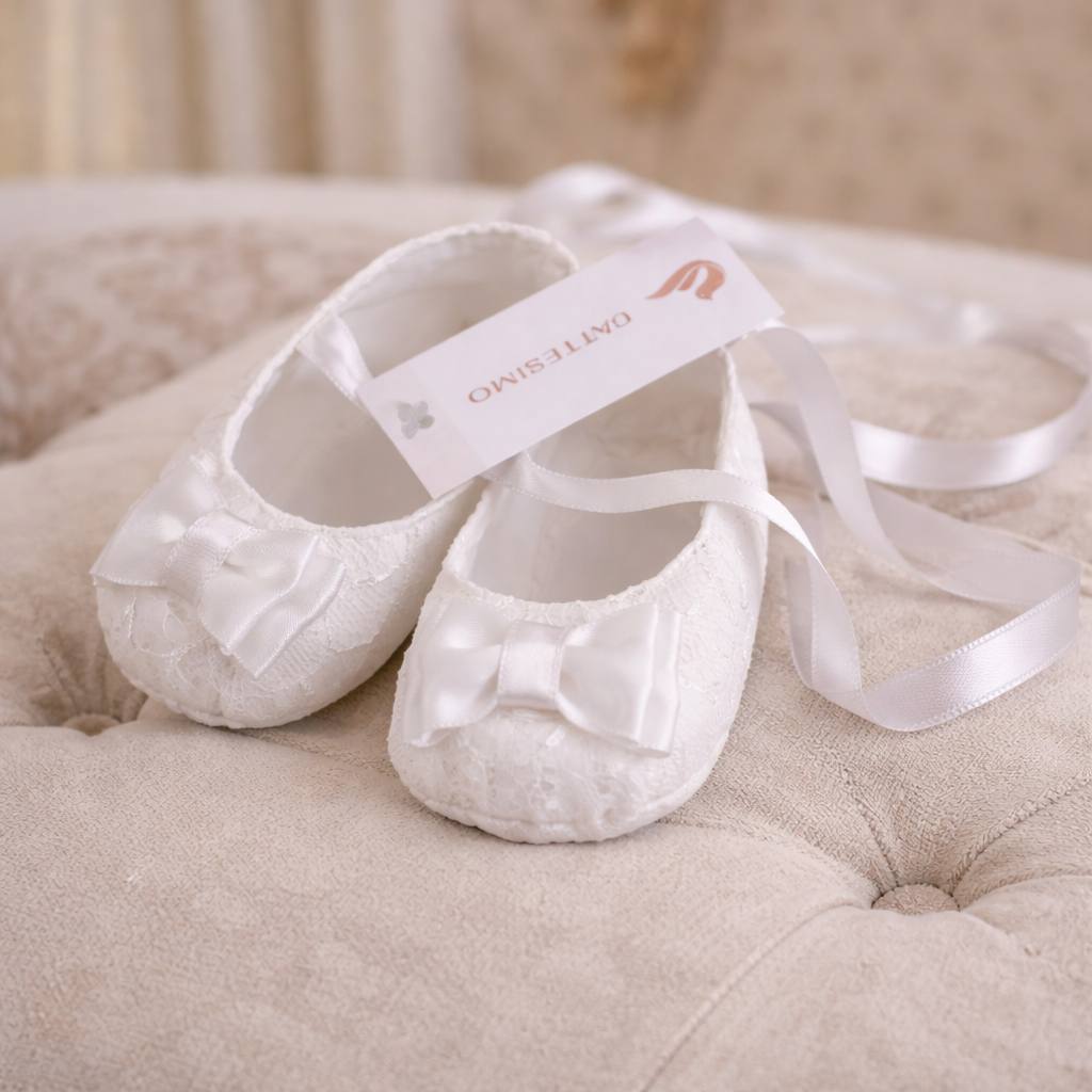 White baby shoes with a ribbon on a beige cushion