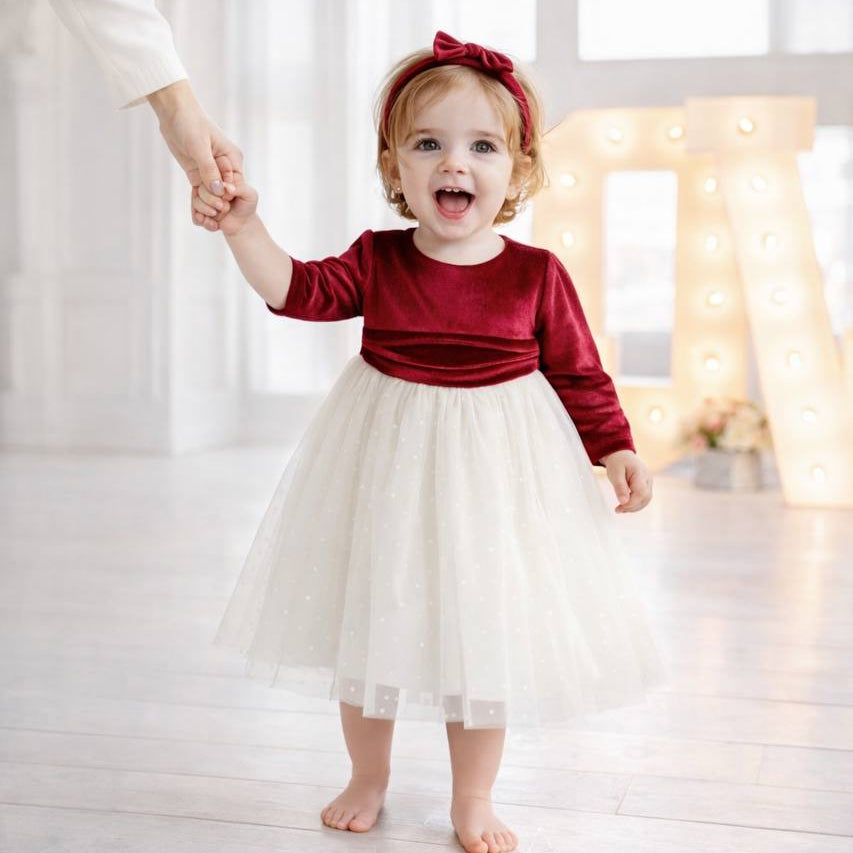 Child in a red top and white skirt standing on a light wooden floor with a blurred background.