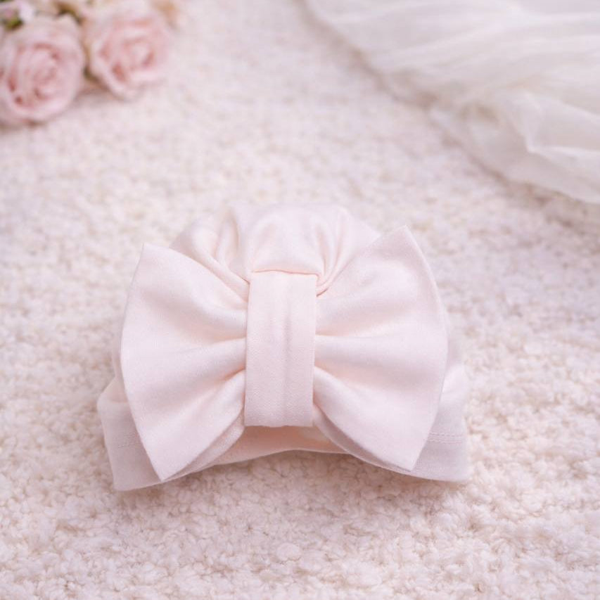 White bow on a textured white surface with pink flowers in the corner