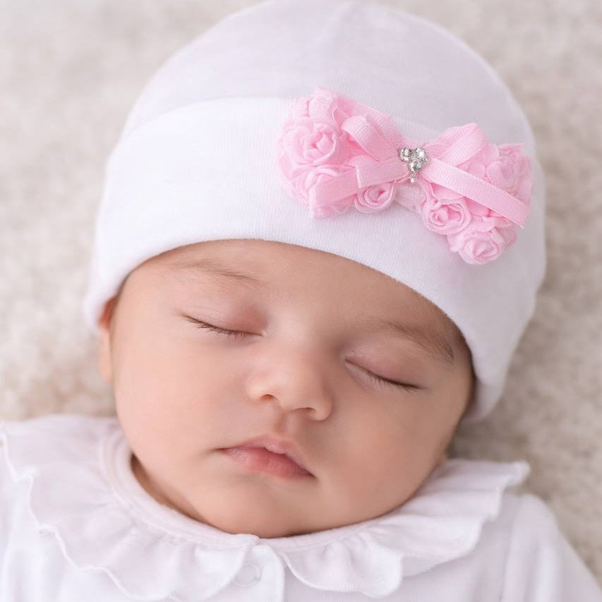 Newborn baby sleeping with a white hat and pink bow on a neutral background