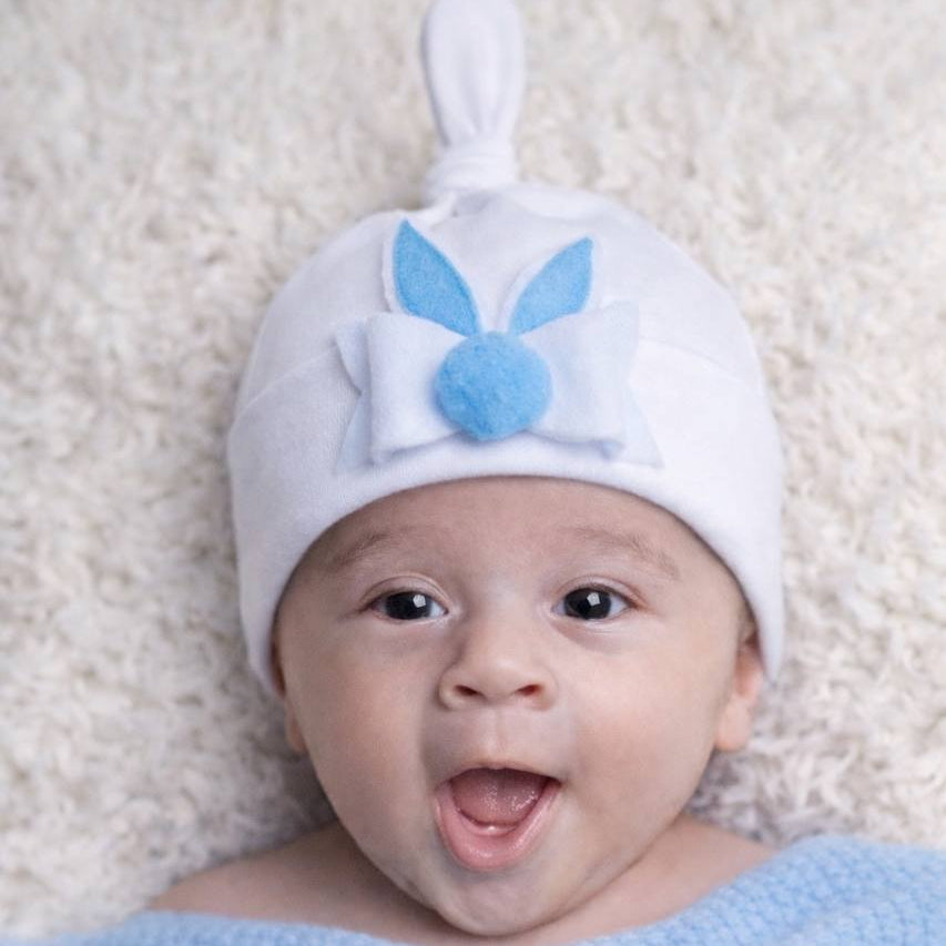 Baby wearing a white bunny hat with blue ears on a light background