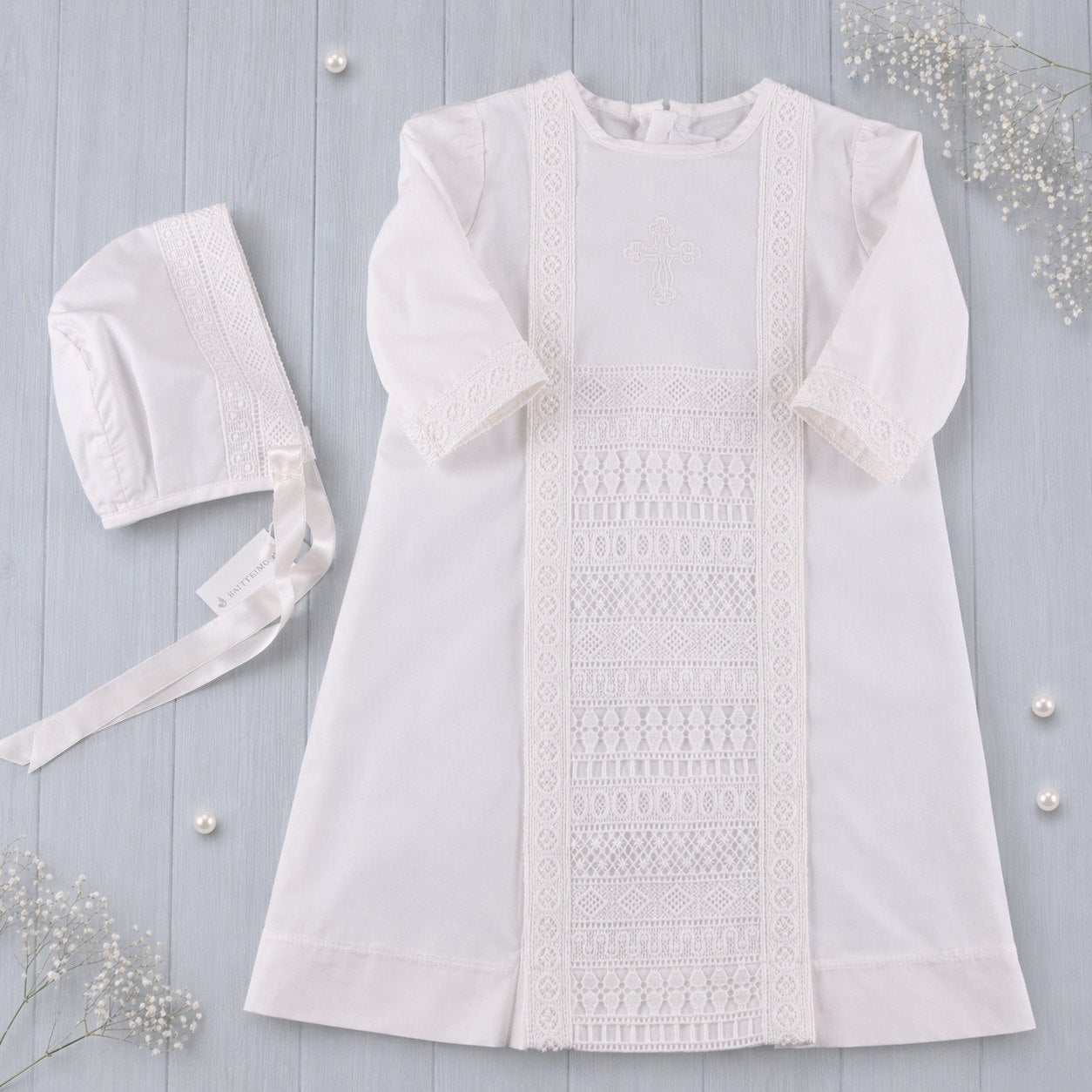 Boys baptism outfit and bonnet on a light gray wooden surface 