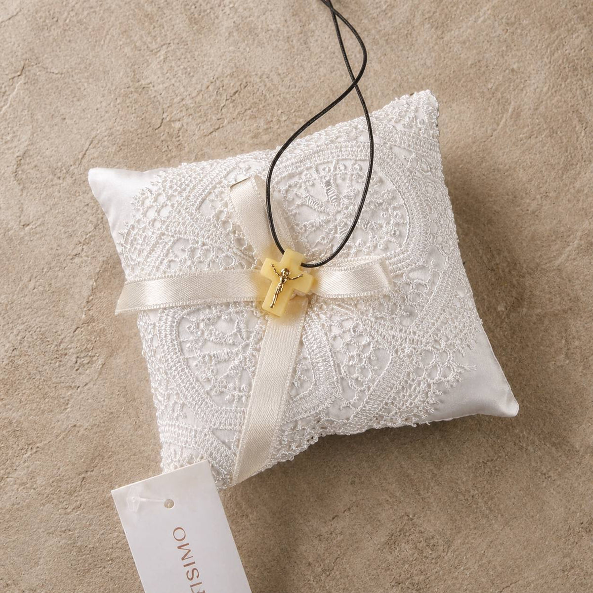 A white satin and lace ring pillow with a cream ribbon bow and a small gold cross charm, shown on a textured beige background with a brand tag reading OWISIMO.