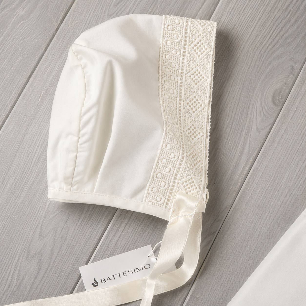 White baby bonnet with lace details on a gray wooden surface