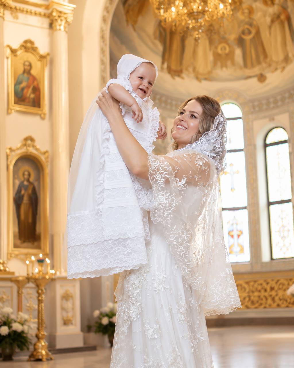 Woman in a white lace dress holding a baby in a church setting