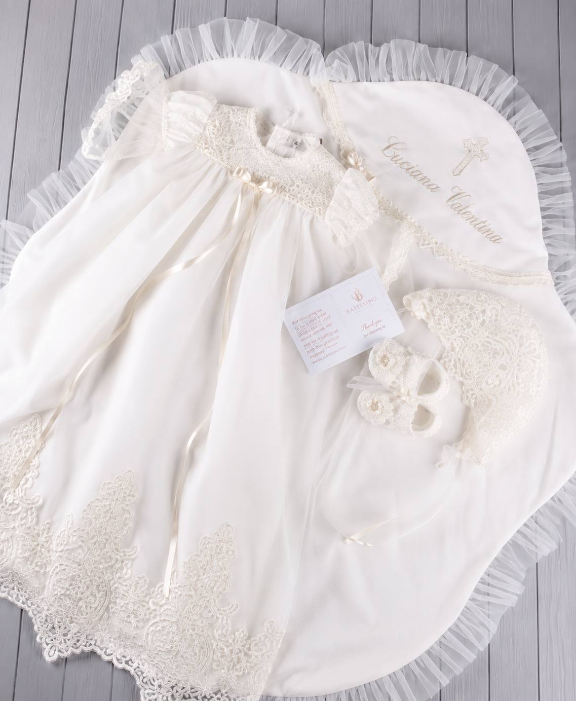 An ivory baby christening outfit set laid flat on a christening blanket background. 