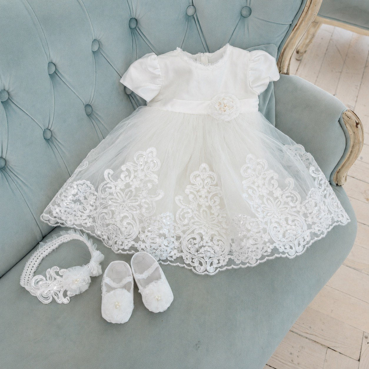 A white baby girl's baptism dress with short puff sleeves, a lace-trimmed tulle skirt, and a matching white lace headband and small white shoes