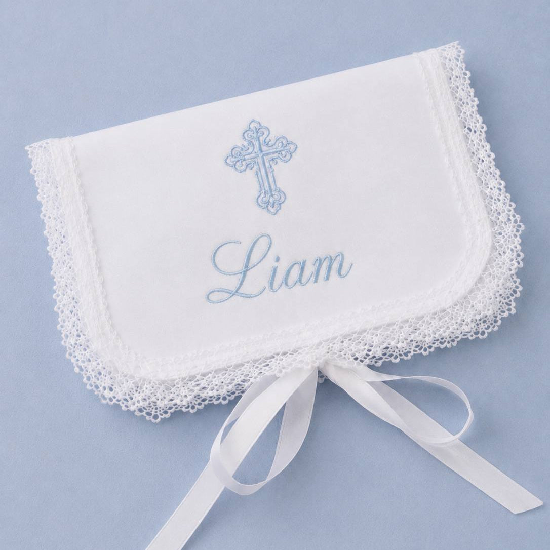 A white embroidered baby baptismal Baptism First Curl Keepsake with lace trim, featuring a light blue cross, the name 'Liam' in script, and a white satin ribbon tied at the bottom, displayed on a light blue background.