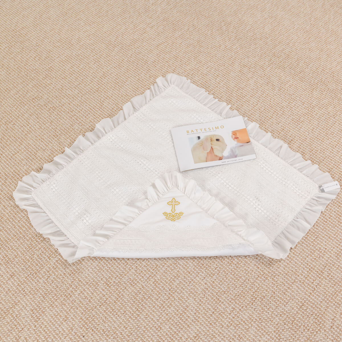 White baby blanket with ruffled edges and a cross emblem on a beige surface