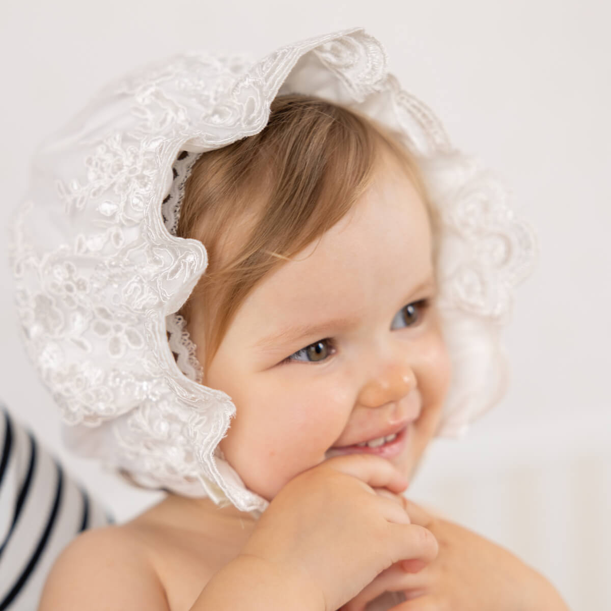 Child wearing a white lace bonnet with a plain background