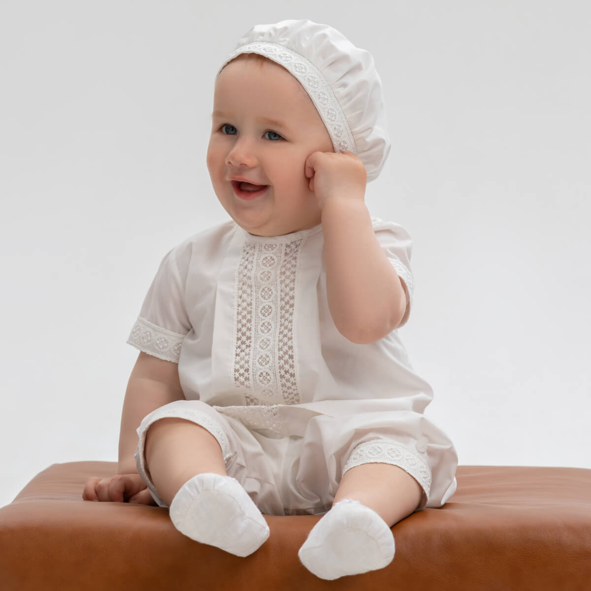 Baby in a Baby Boy Baptism Suit with lace details sitting on a brown surface against a light gray background