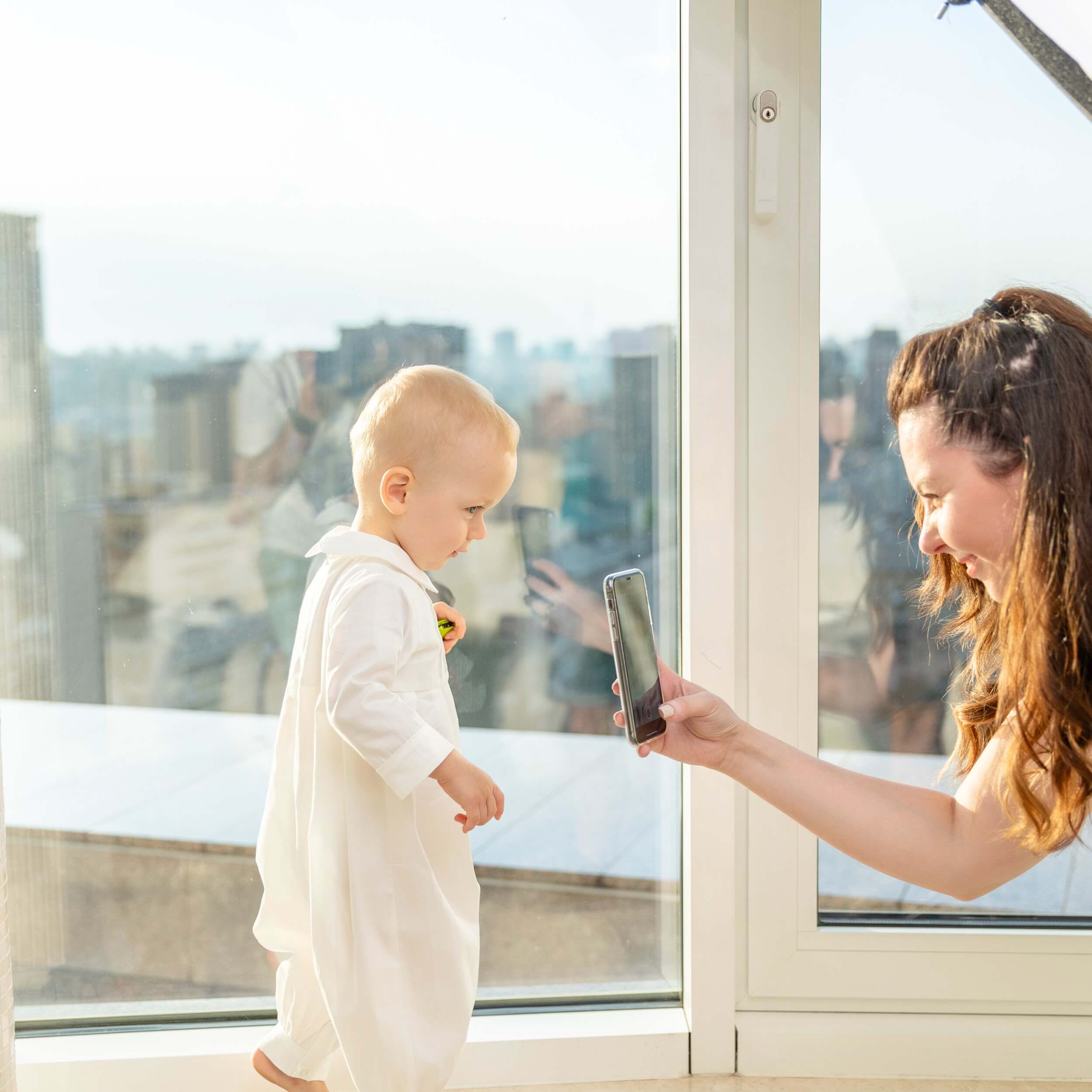  Child in Baby Boy Baptism Bubble Romper by a large window with a cityscape view.