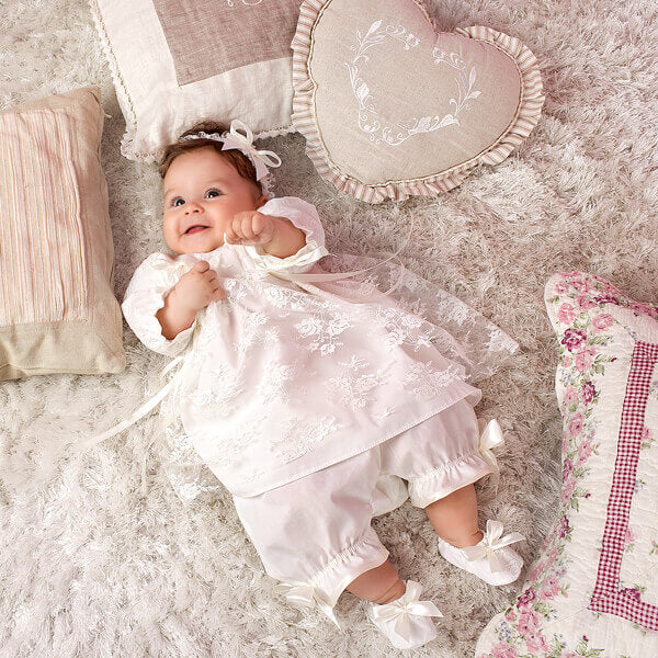 Baby in a Lace Baptism Set for Baby Girl lying on a soft surface with decorative pillows.