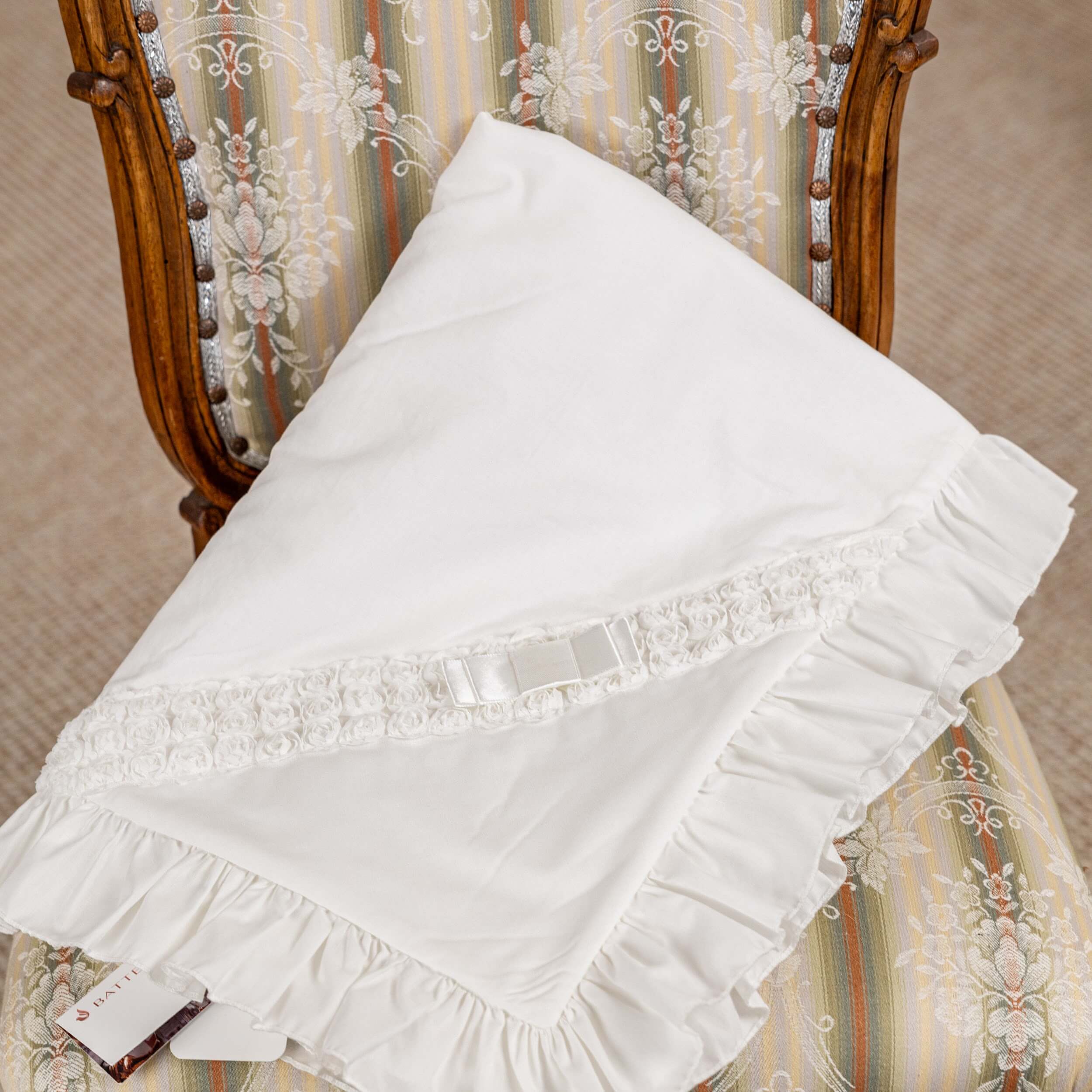 White lace-trimmed christening blanket  on a decorative chair with striped fabric.
