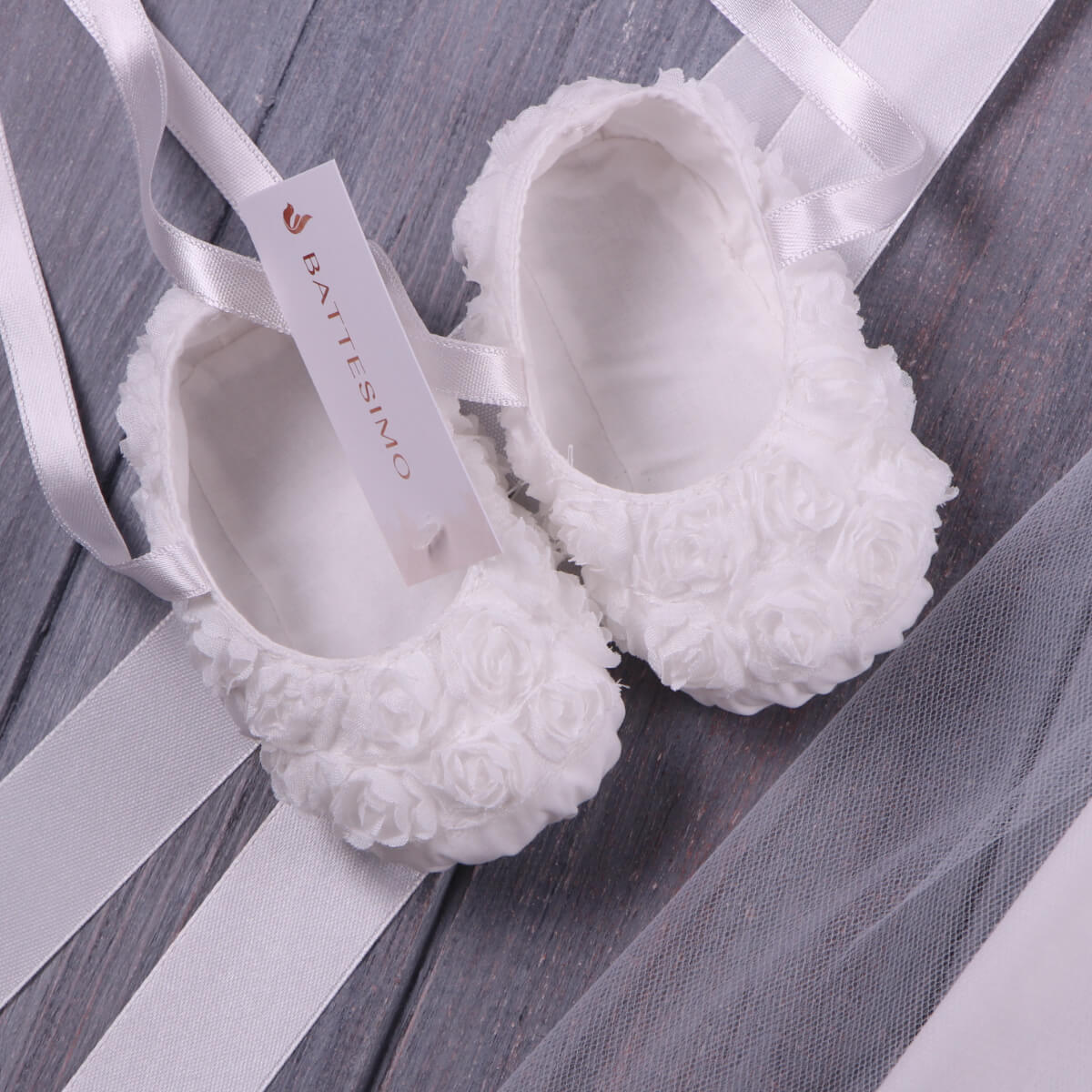 Christening Booties with fluffy sole on a wooden surface, featuring the brand 'Battilino'.