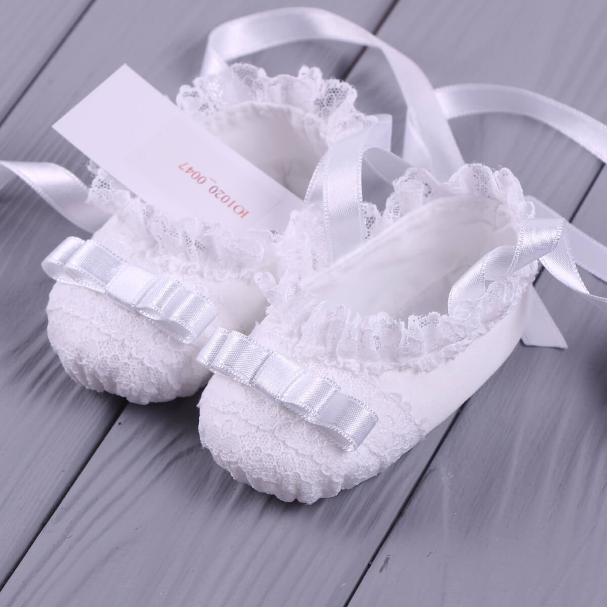 Christening Booties with lace details and ribbons on a gray wooden surface